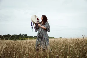 Sophie Messager standing in a meadow holding a drum